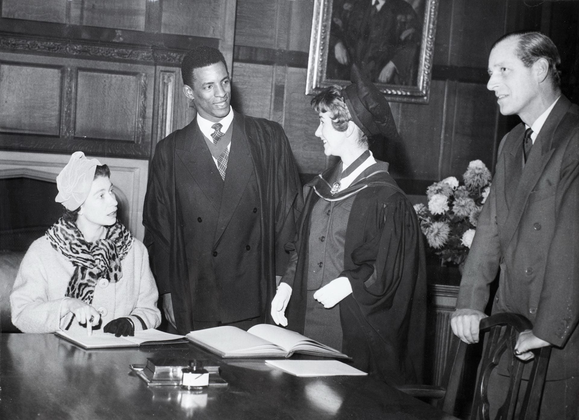 George Odlum stands at a table with Queen Elizabeth II seated at the table on a visit to the University of Bristol